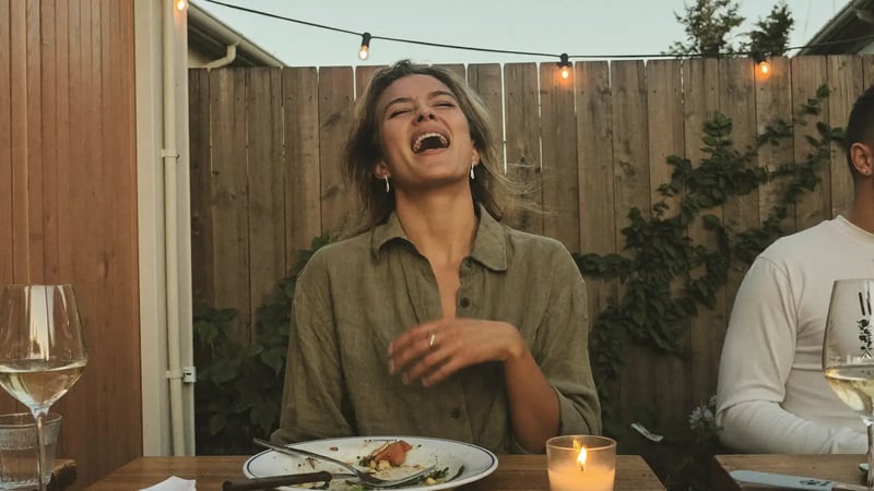 woman laughing with her head tilted back at a backyard dinner with friends as a candid dating photo example