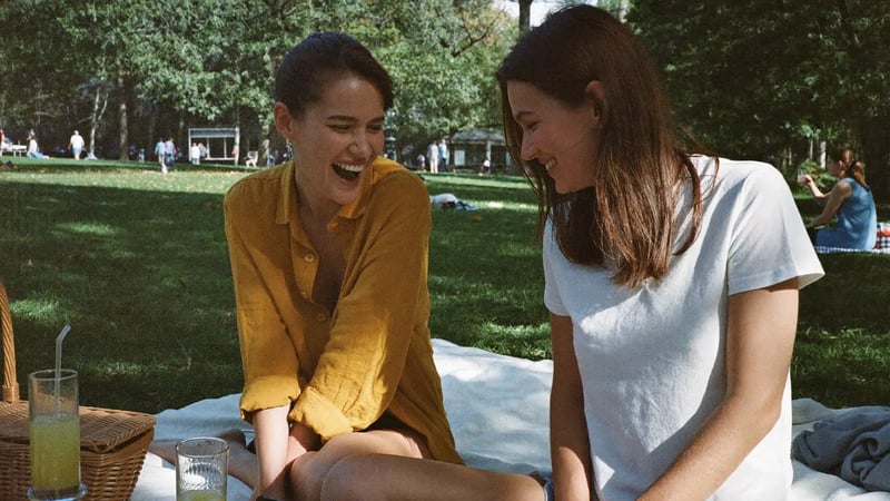 two women laughing together on a picnic blanket in a park as a social dating profile photo example