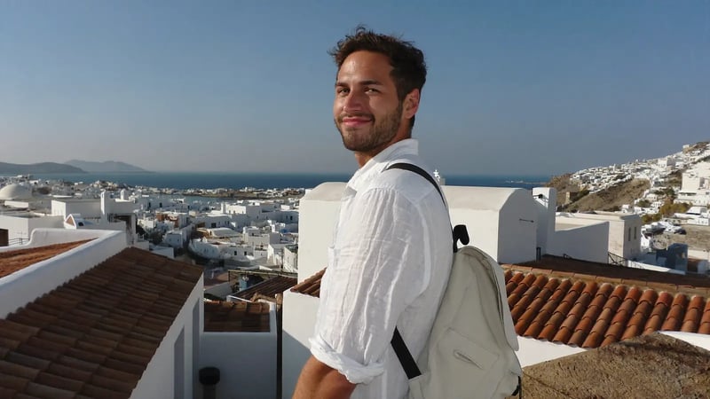 man in a white linen shirt at a viewpoint above a white coastal town and blue sea as a travel dating photo example